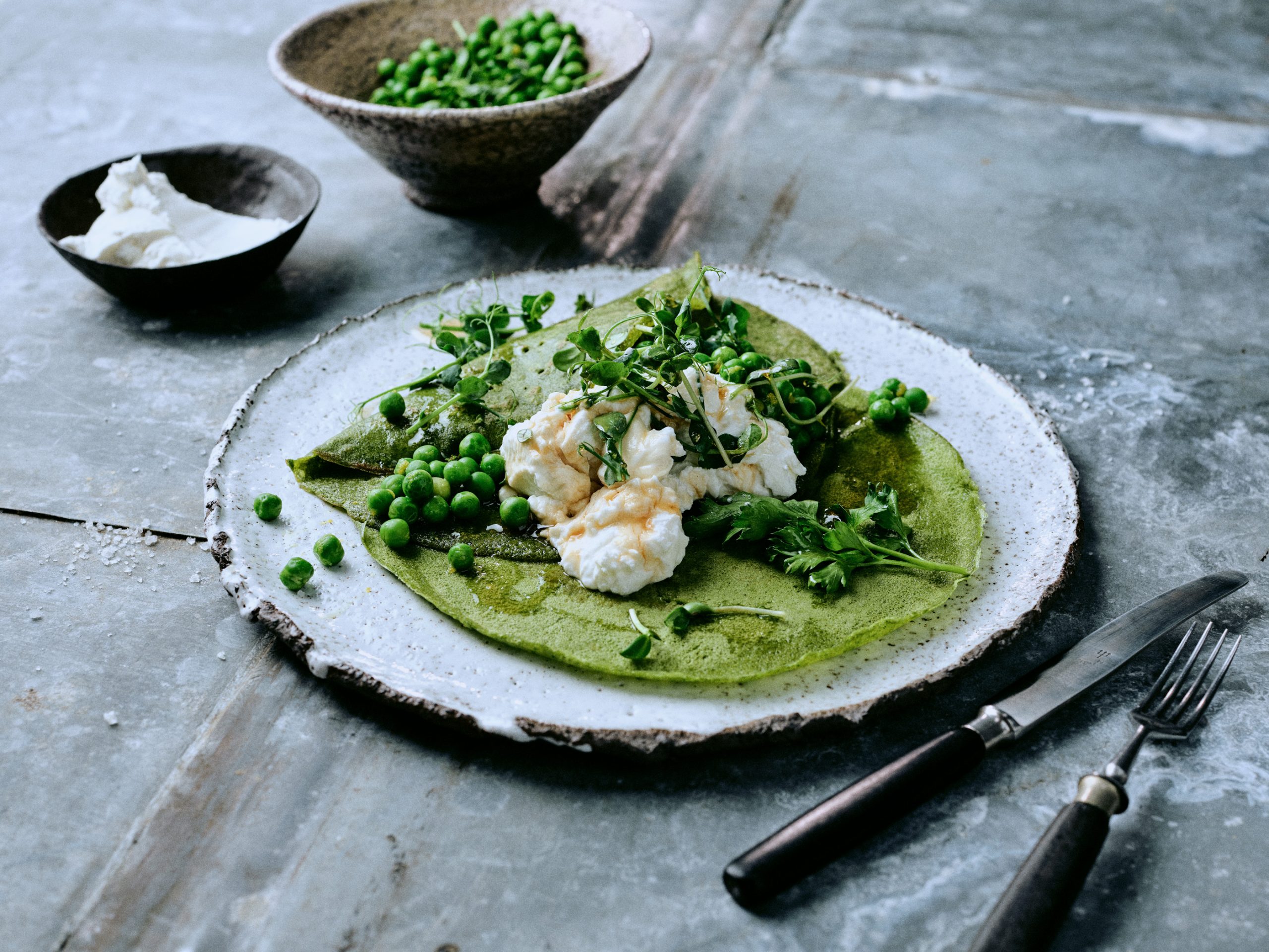 Foto von Spinat-Crepes mit Ziegenquark und Erbsen-Salat mit einer Schale Erbsen daneben - vegetarisches Rezeptfoto der querbeet Ausgabe von taste appeal– dem Foodmagazin