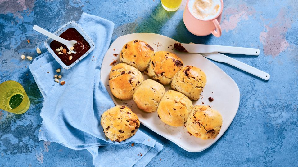 Totale, Vogelperspektive von TASTE APPEAL– Rezept: Schoko-Quarkbrötchen mit Schokonussaufstrich, daneben Besteck, gelbe Gläser und pinke Tasse