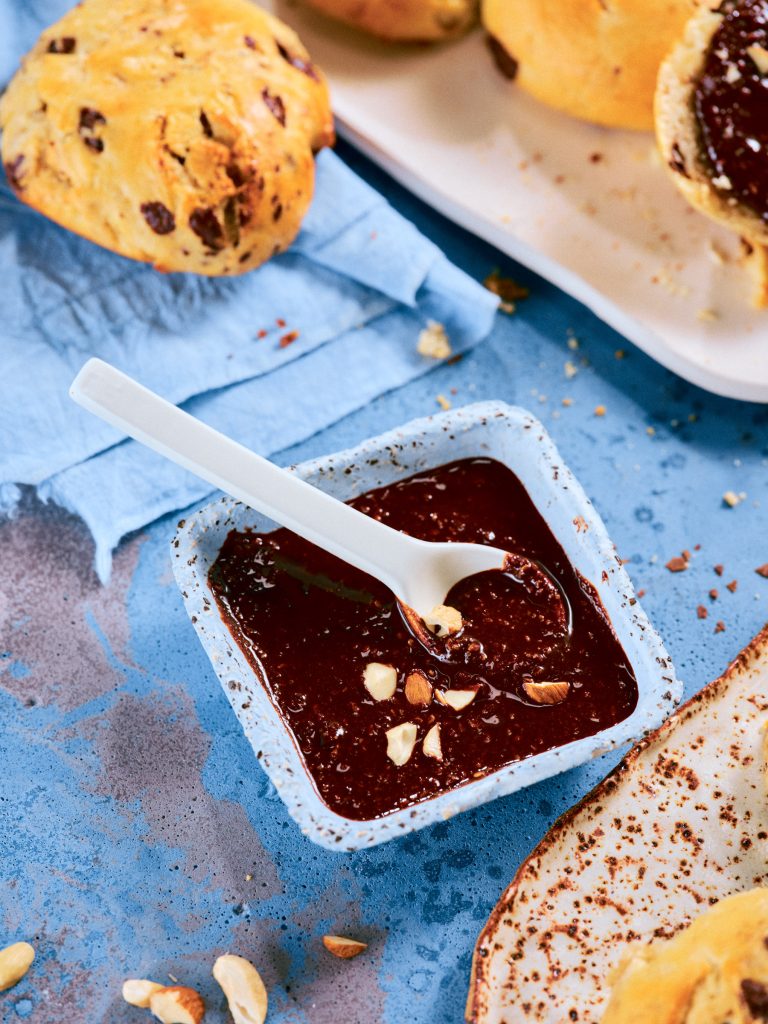 Detailaufnahme von TASTE APPEAL– Rezept: Schoko-Quarkbrötchen mit Schokonussaufstrich, Fokus auf Schokoaufstrich in kleiner Schale mit Löffel