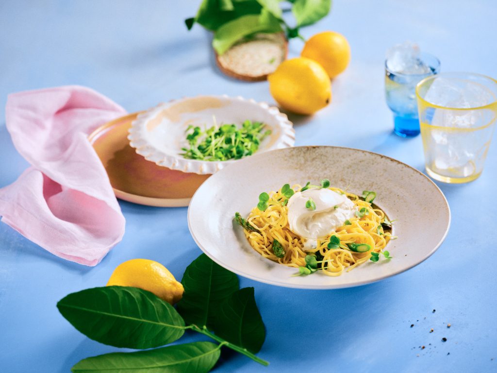 Totale von TASTE APPEAL– Rezept: Pasta mit Zitrone, Spargel und Burrata, im Hintergrund kleiner Teller mit Kresse, im Vordergrund Zitrone mit Blätter