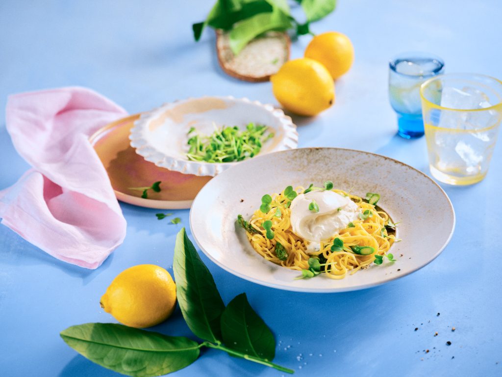 Totale von TASTE APPEAL– Rezept: Pasta mit Zitrone, Spargel und Burrata, im Hintergrund kleiner Teller mit Kresse, im Vordergrund Zitrone mit Blätter