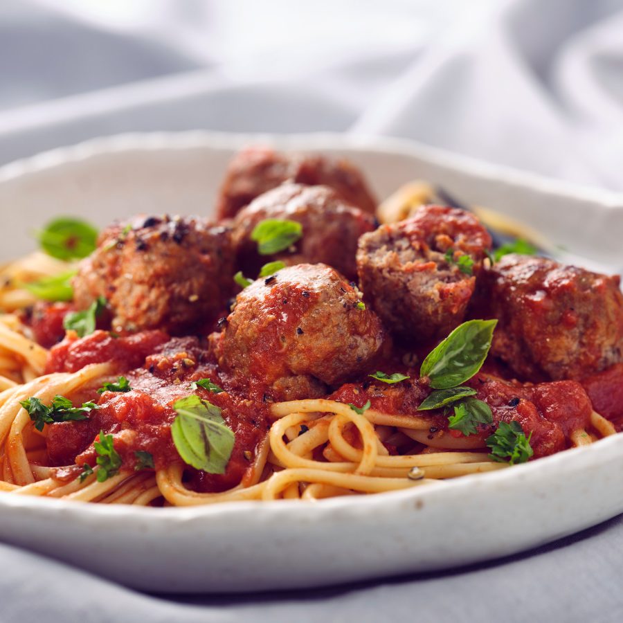 Nahaufnahme von TASTE APPEAL– Rezept Grandmas Meatballs auf hellem Teller, mit schwarzem Besteck, von der Seite