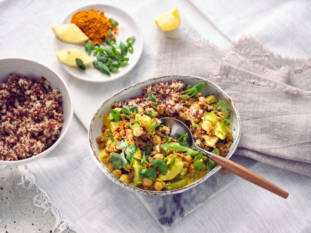 Totale von TASTE APPEAL– Rezept Schmorgurkencurry mit Sonnenblumenhack in Schüssel, im Hintergrund kleiner Teller mit Zitrone, Currypuler und Frühlingszwieblen