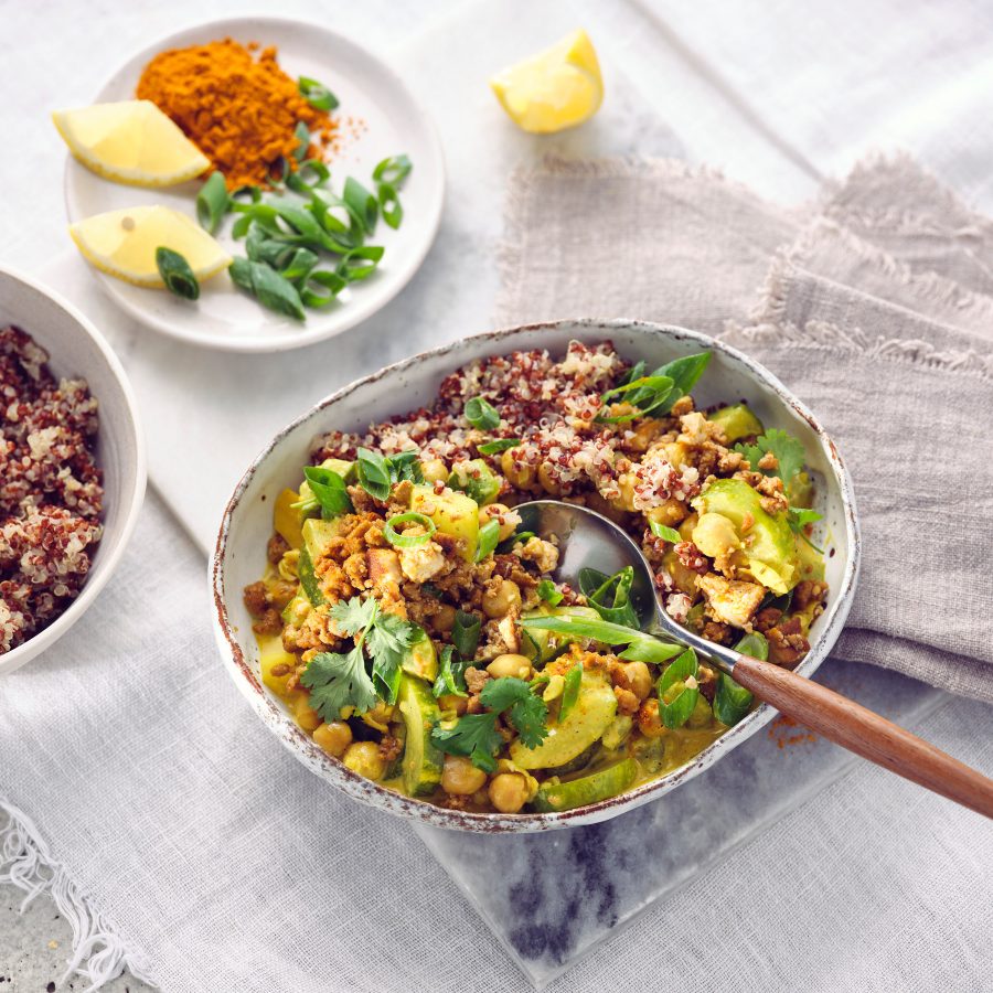 Totale von TASTE APPEAL– Rezept Schmorgurkencurry mit Sonnenblumenhack in Schüssel, im Hintergrund kleiner Teller mit Zitrone, Currypuler und Frühlingszwieblen