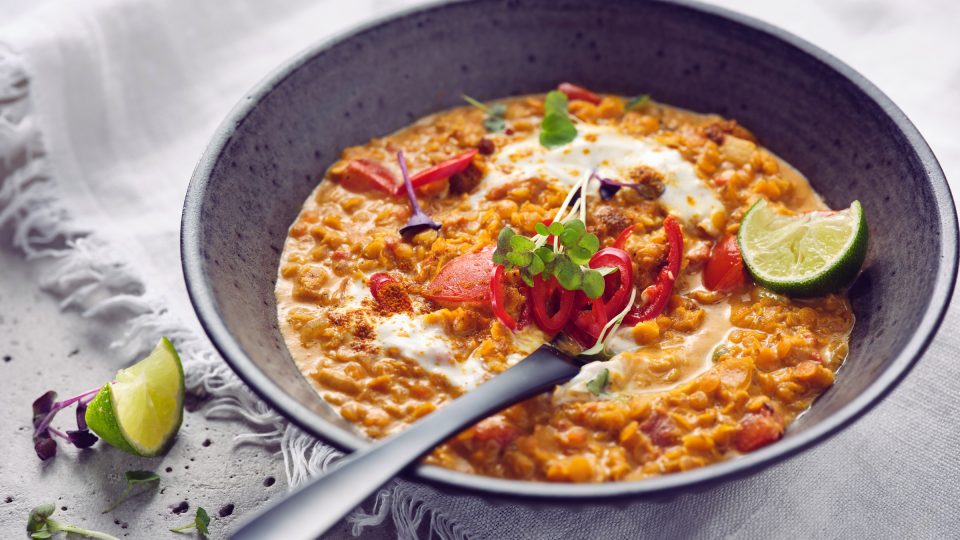 Nahaufnahme von TASTE APPEAL– Rezept Vegane Rote Linsensuppe mit Kokosmilch, in dunkler Schüssel mit Besteck