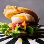 Großaufnahme von TASTE APPEAL– Rezept Breakfast-Burger mit Deichkäse und pochiertem Ei auf gestreiften Podest