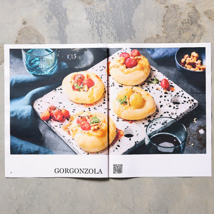 TASTE APPEAL– Ausgabe "käseblatt" aufgeschlagen mit Mini Pizza Rezept auf grau Steinuntergrund