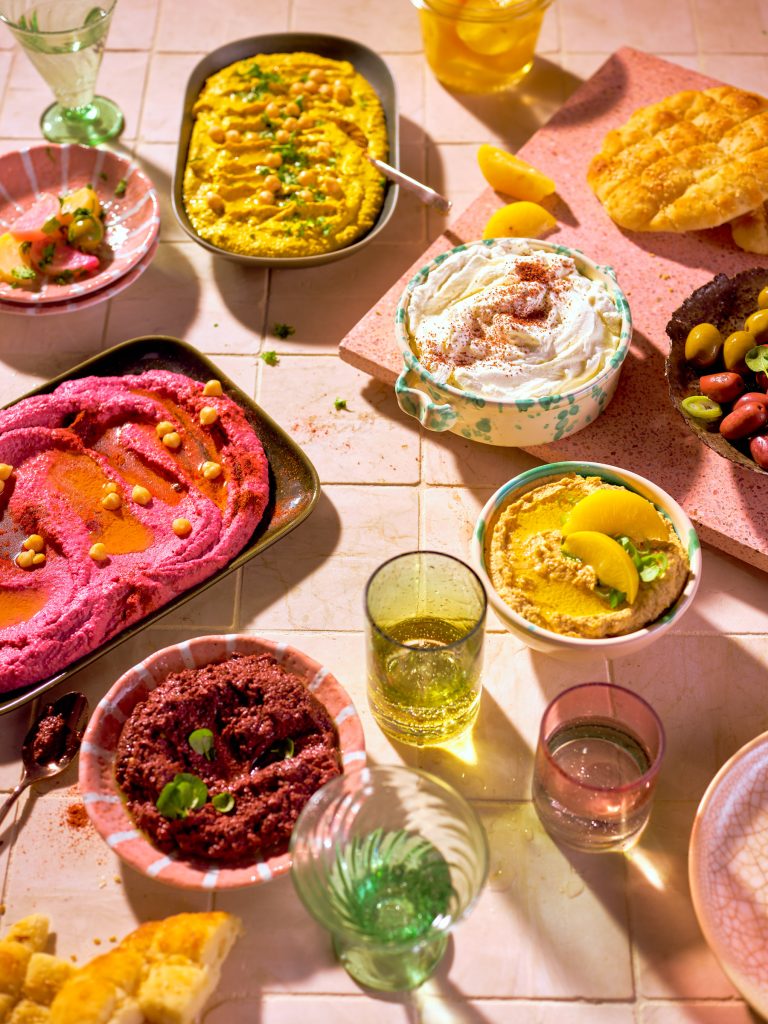 Totale von TASTE APPEAL– Rezept Laffa-Brot auf pink Steinplatte, neben Oliven in Schüssel, Hummus in drei Varianten und Gläsern
