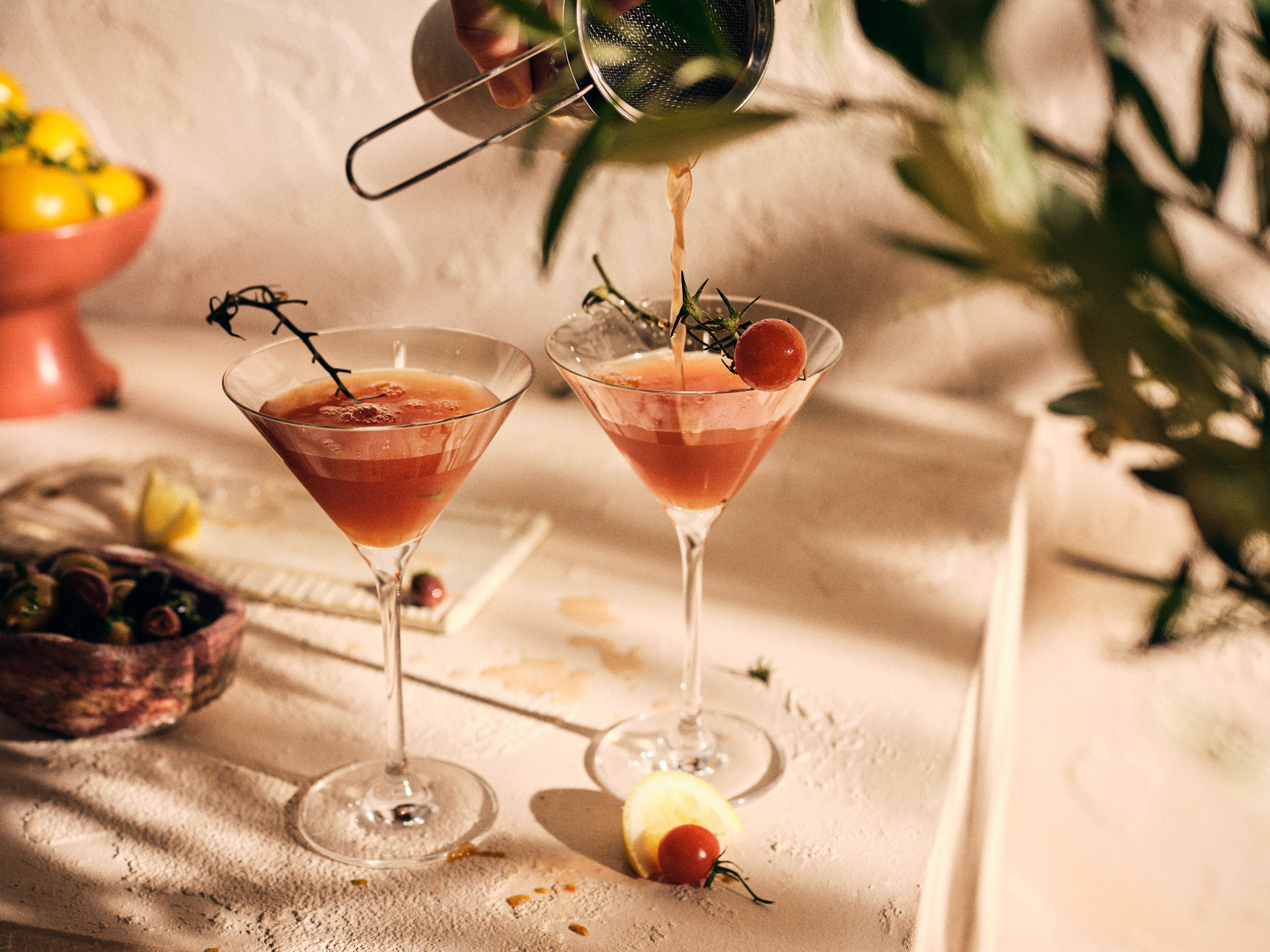Totale von TASTE APPEAL– Rezept Tomaten-Martini mit Tomatenessenz im sommerlichen Setting, Hand schüttet Martini aus Shaker ein