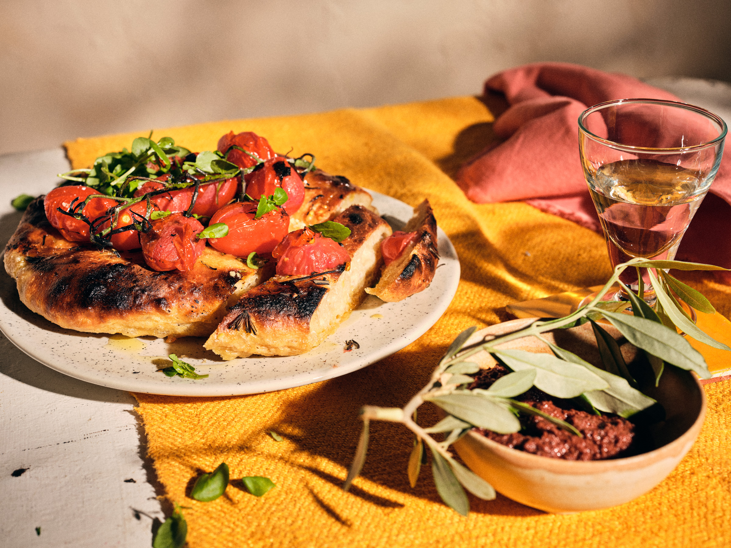 Halbtotale von TASTE APPEAL– Rezept Tomaten-Pfannenbrot mit Burned-Tomatos und Kresse, im Vordergrund Pesto mit Olivenzweig