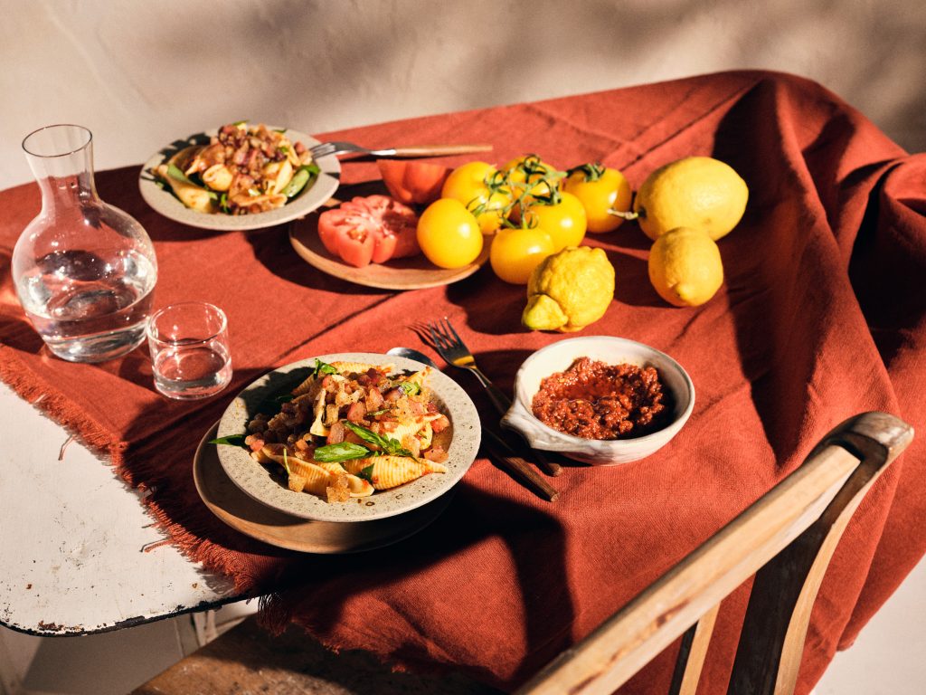 Totale von TASTE APPEAL– Rezept Tomaten-Pesto mit Rauchmandel und Chili in beigem Teller, daneben Pesto in Schüssel im Hintergrund Zitronen und Tomaten