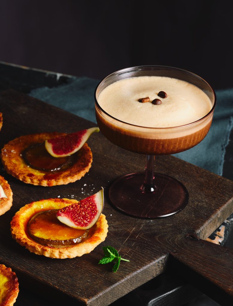 TASTE APPEAL- Rezept Espresso Martini neben Mini-Birnen-Kurkuma-Tarte auf dunklem Holzbrett